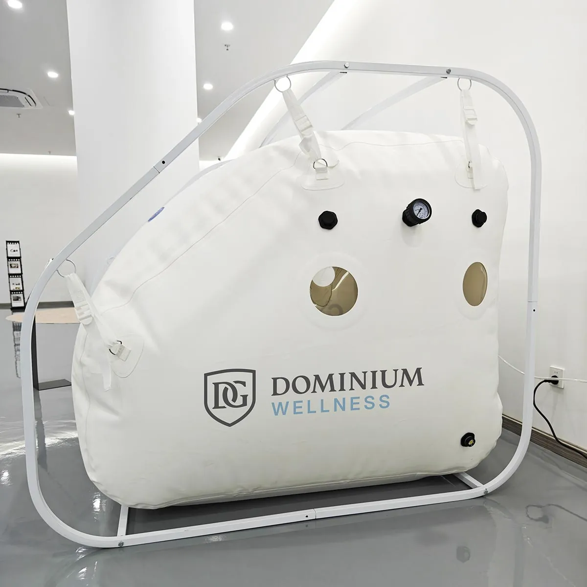 Modern, minimalist bir odada büyük, beyaz “Dominium Wellness” DW160MS model hiperbarik kabin. Kabinin şeffaf pencereleri ve basınç göstergeleri var.
