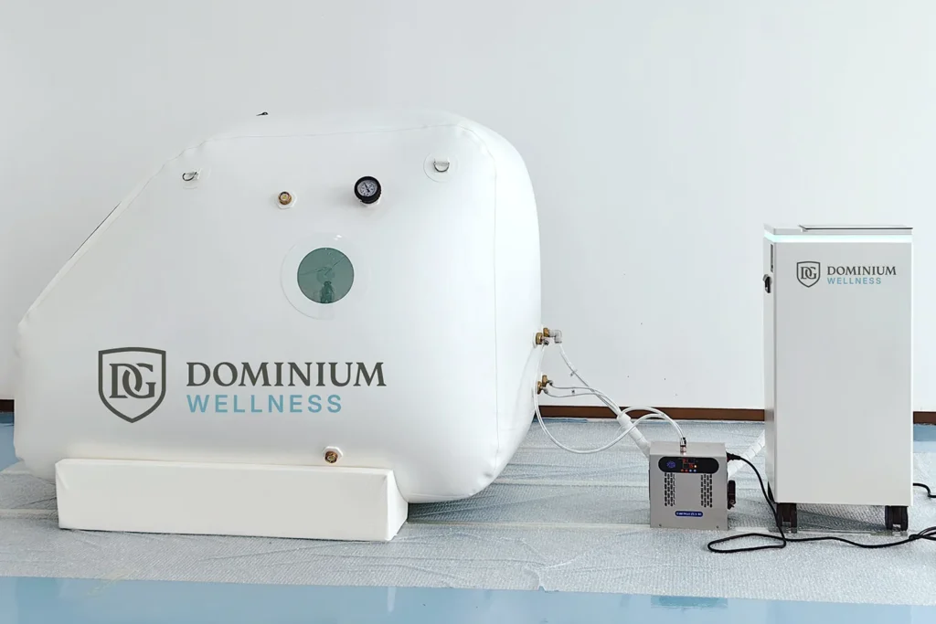 Göstergeleri ve yan penceresiyle, kontrol ünitesine bağlı “Dominium Wellness” DW160MS model beyaz hiperbarik kabin; şık, medikal ve modern bir ortam.