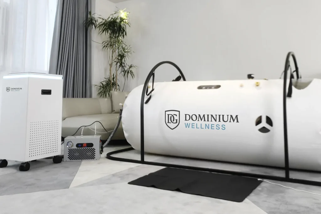 Şık, modern bir odada “Dominium Wellness” DW220ML model beyaz hiperbarik kabin. Yakınında hava filtreleme ekipmanı ve saksı bitkisi, dingin bir wellness atmosferi oluşturuyor.