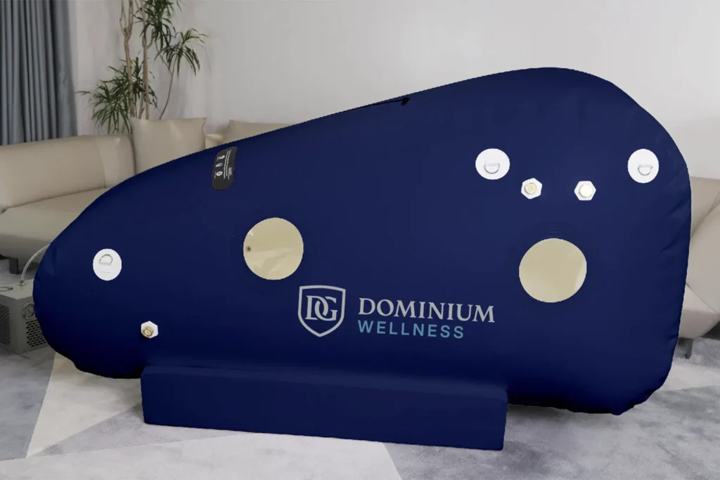 Modern bir odada “Dominium Wellness” DW220MLS model mavi hiperbarik kabin. Bej kanepeler ve saksı bitkisiyle çevrili; sakin, terapötik bir ambiyans.