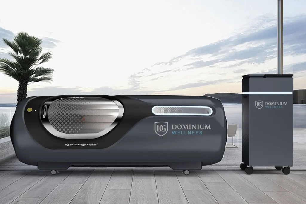 Deniz kenarında “Dominium Wellness” etiketli DW230TKLP model şık hiperbarik oksijen kabini. Modern tasarım, palmiye ağacı ve gün batımı gökyüzü dingin bir atmosfer yaratıyor.