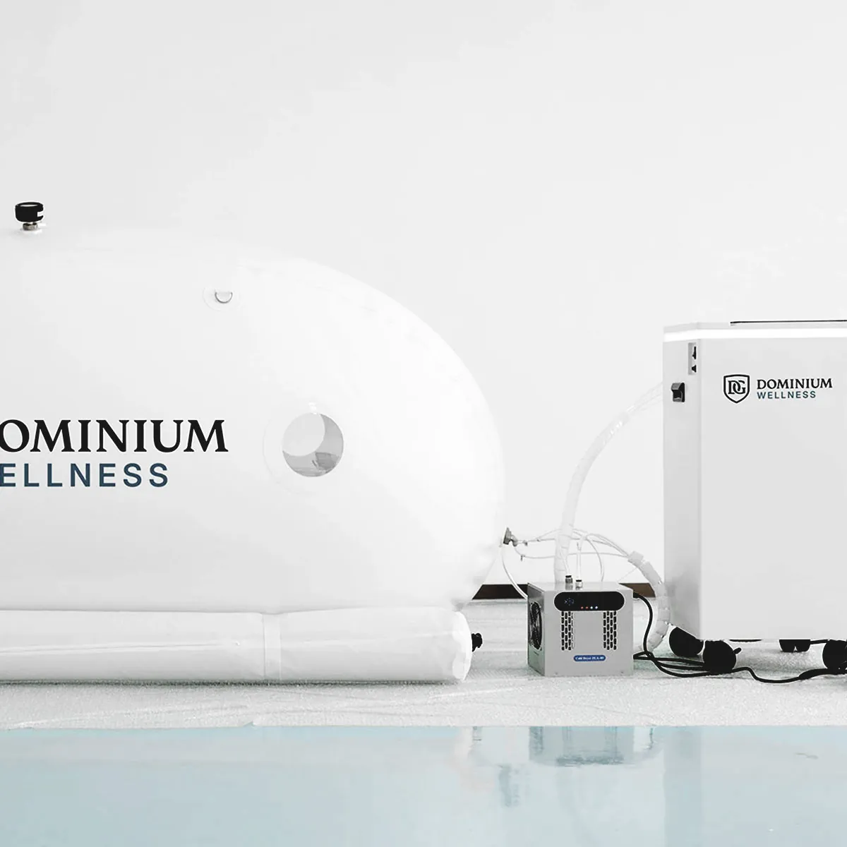 Bir kontrol ünitesine bağlı şık, beyaz “Dominium Wellness” DW240MDO model hiperbarik kabin. Aydınlık, minimalist ortam modern wellness teknolojisi hissi veriyor.